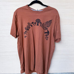 the front of a rust brown t-shirt printed with an arch of black mushrooms and a fern across the chest.