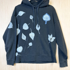 Front of black hoodie with white leaf prints and denim leaf printed patch on left breast.