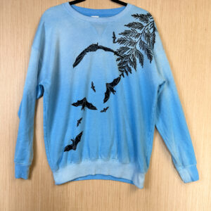 Front of light blue crewneck fading to lighter color around collar with black cedar branch and bat print.