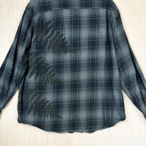 Back of black and grey plaid flannel shirt with three dark brown ferns printed growing out of left side seam.