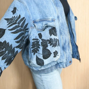 Size S-M woman wearing an oversized denim jacket printed with leaves and ferns on sleeve and front pocket.