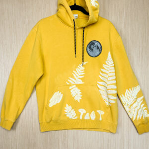 Front of yellow sweatshirt with grey denim patch on left breast, printed with a moon in white ink, ferns on sleeves and pocket, with mushrooms printed in pocket.