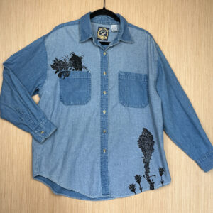 Front of two-toned blue denim shirt printed with a pika in the right breast pocket, beargrass and three Indian paintbrush growing up from left hem.