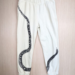 Sand-colored sweats with black snake print with tail at right hip, body looping to bottom edge of right leg, top third and head angled from inseam of left leg, printed up the leg.