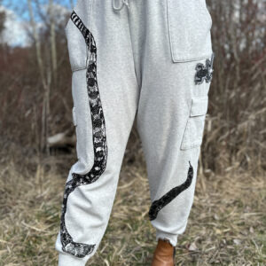 Front of grey sweats printed with black snake print with tail at right hip, body looping to bottom edge of right leg, top third and head angled from inseam of left leg, printed up the leg. Black frog printed on denim patch sewn onto left hip.