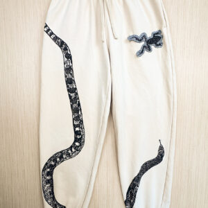 Sand-colored sweats with black snake print with tail at right hip, body looping to bottom edge of right leg, top third and head angled from inseam of left leg, printed up the leg. A frog printed denim patch is sewn onto left hip.