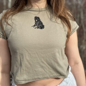 Woman wearing light green cropped t-shirt with black toad printed high at center chest.