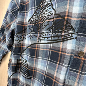 Closeup of black steelhead tail printed on blue and orange plaid shirt.