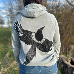 Back of woman wearing long light blue hoodie with life-size black-billed magpie with wings spread printed at an angle across the back.
