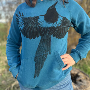 Woman wearing fitted blue sweatshirt with black ink magpie printed with wings spread across the chest, with left wing wrapping into the armpit.