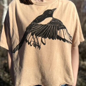 Woman wearing tan shirt with flapping magpie print across chest.