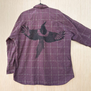 Back of red/gold checked button down with black-billed magpie printed with its wings spread, small crease printed in its head/shoulders, one small magpie primary feather printed near side seam on right side.