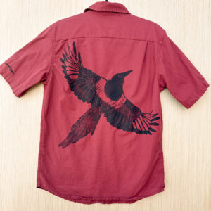 Back of red short-sleeve button down with black-billed magpie printed with wings spread across the back at an angle, flying to the right.