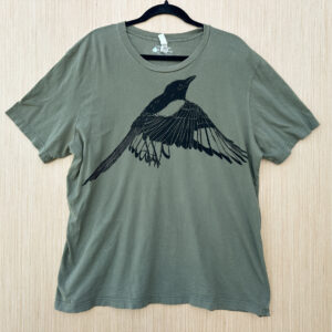Front of olive green short sleeve t-shirt printed with flapping black-billed magpie printed in black ink at an angle across chest.