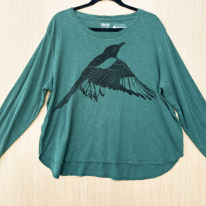 Front of teal long-sleeve t-shirt printed with flapping black-billed magpie printed in black ink at an angle across chest.