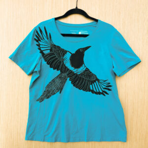 Front of bright blue t-shirt with black-billed magpie printed at an angle across the chest with its wings spread.