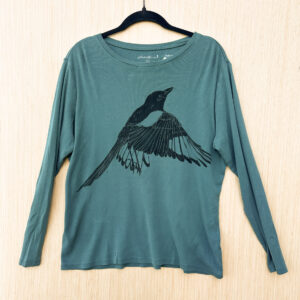 Front of teal long-sleeve t-shirt with life-size flapping magpie printed in black ink across chest.