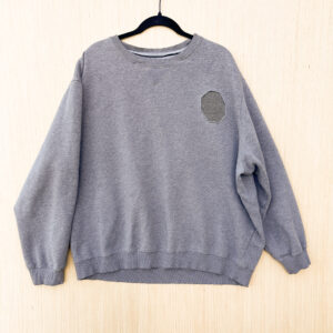 Front of heathered grey crewneck sweatshirt with slightly darker grey octagon reverse appliqué at left breast.
