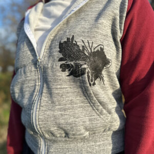 Closeup of pika printed coming out of pocket on grey hoodie with red sleeves, pictured with leaves in its mouth.