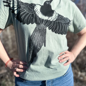 Woman wearing a green t-shirt with a life-size black-billed magpie printed with wings spread across the chest.