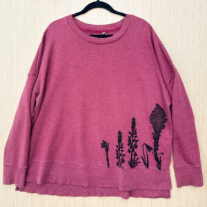 Front of berry colored sweatshirt with ghost pipe, lupine, yellow bell, and beargrass printed growing up from left hem in black ink.