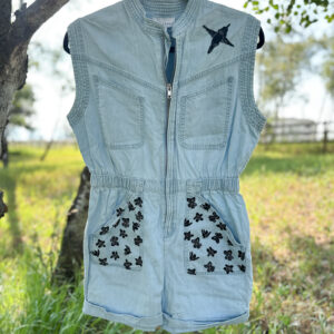 Front of short blue denim romper with tiny flowers printed on the short pockets, hummingbird printed on left shoulder.