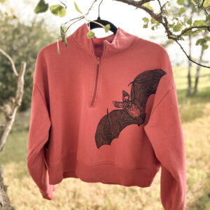 Front of cropped pink quarter zip sweatshirt with black pallid bat printed diagonally across the front from the right shoulder.